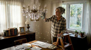 Homeowner dusts crystal chandelier in sunlit room