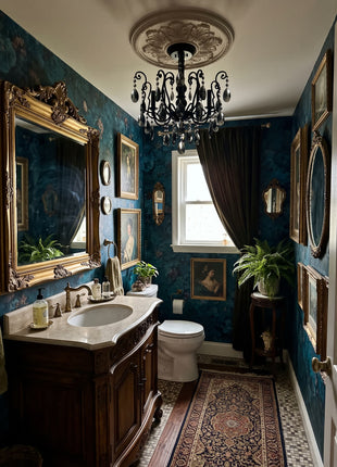 A luxurious vintage-style bathroom featuring deep blue patterned wallpaper, an ornate gold-framed vanity mirror, a dark wood sink cabinet, a white toilet, a patterned area rug, and a black crystal chandelier hanging from a decorative ceiling medallion.