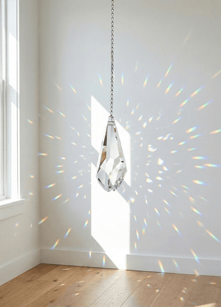 Swarovski Crystal hanging from a chain casting rainbow patterns on a white wall.