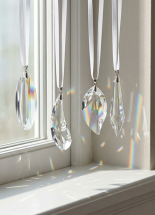 Crystal prisms hanging by ribbons on a windowsill with sunlight casting rainbow colors.