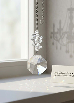 Swarovski Crystal octagon prism hanging on a chain with a card in front of a window.