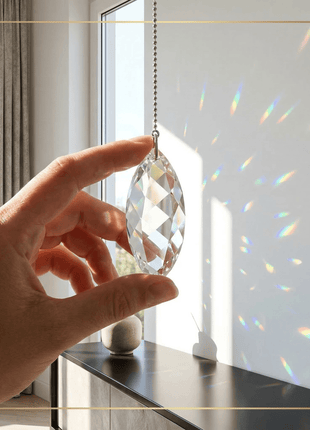 Hand holding a Swarovski  crystal prism in front of a window with rainbow