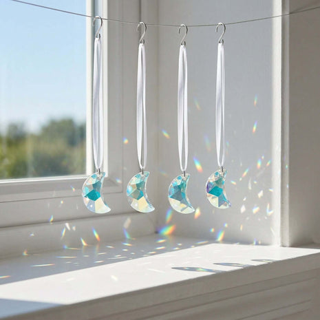 Swarovski Crystal moon phase decorations hanging by a window with sunlight casting shadows.