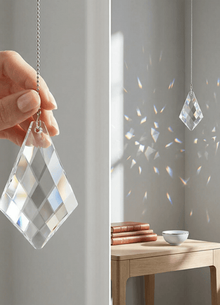 Crystal suncatcher hanging from a hand with sunlight casting patterns on a wall.