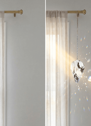 Sheer curtains with a crystal hanging ornament in front of a light gray wall.