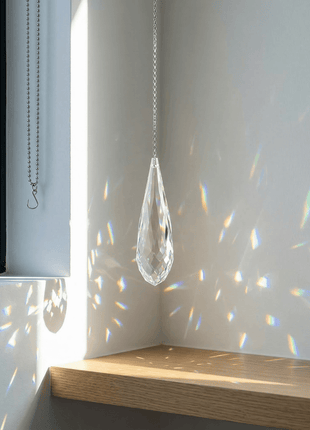 Crystal teardrop hanging from a chain with rainbow on a white wall.