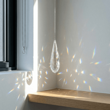 Crystal teardrop hanging from a chain with rainbow on a white wall.