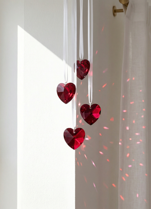 Red heart-shaped decorations hanging in front of a window with a light pink projection on the wall.