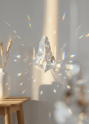 Crystal prism casting rainbow colors on a wall with a vase of wheat in the foreground.