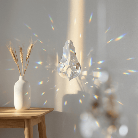 Crystal prism casting rainbow colors on a wall with a vase of wheat in the foreground.