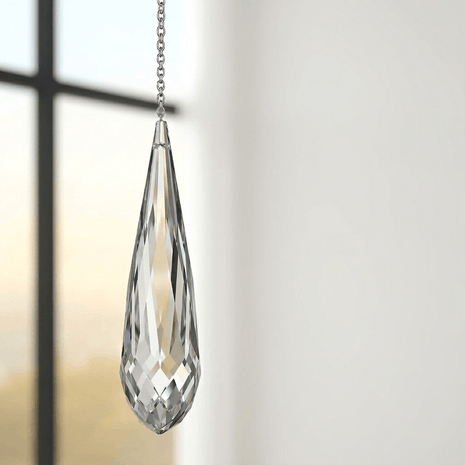 Clear teardrop-shaped Swarovski crystal hanging against a neutral background