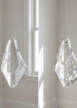 Two Swarovski crystal prisms hanging in front of a window with sunlight filtering through.
