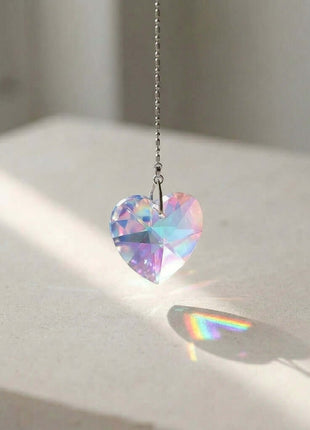 Heart-shaped Swarovski crystal pendant on a chain with rainbow colors, casting a shadow on a light surface.