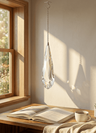 Crystal chandelier hanging above a wooden table with an open book, cup, and small plant.
