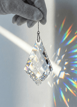 Crystal prisms hanging from a gloved hand with rainbow colors on a gray background