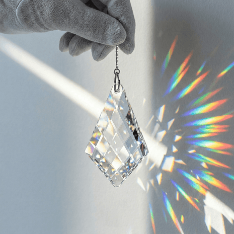 Crystal prisms hanging from a gloved hand with rainbow colors on a gray background