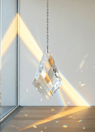 Crystal prism hanging by a chain with sunlight casting rainbow colors on a window.