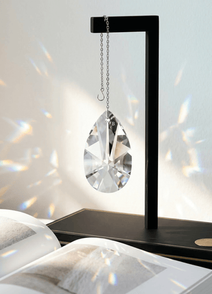 Decorative crystal hanging from a black stand on a white surface with rainbow