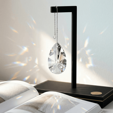 Decorative crystal hanging from a black stand on a white surface with rainbow