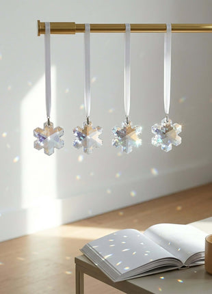 Swarovski Crystal snowflake ornaments hanging on a gold rod with an open book and mug below.