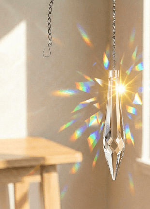 Crystal prisms hanging from a chain, creating rainbow in a room with a table and window.