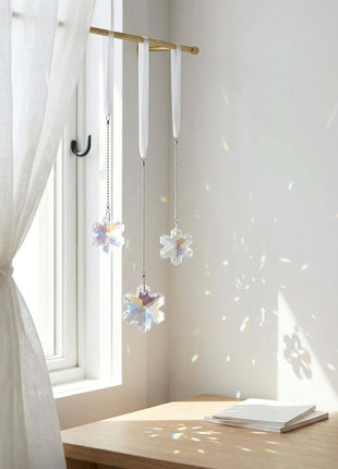 Decorative flower-shaped crystals hanging from a rod in a bright room with white curtains and a wooden desk.