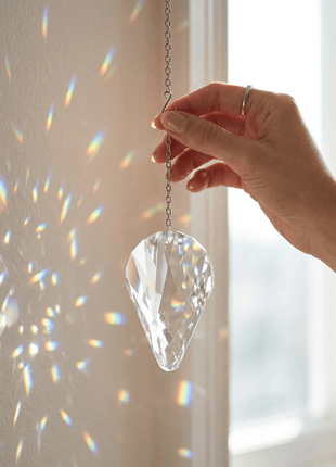 Hand holding a crystal prism against a light background, creating colorful patterns.