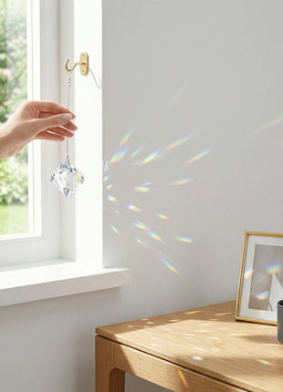 Hand hanging a Swarovski crystal decoration by a window with a cup and frame on a table.