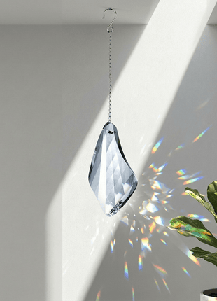 Swarovski Crystal hanging ornament with rainbow, placed next to a potted plant on a plain background
