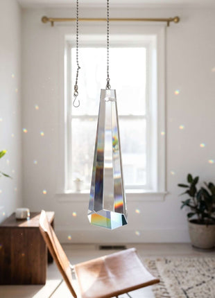 Tall, reflective pendant light hanging in a room with a chair and plants.